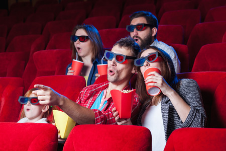 The spectators sitting in the cinema and watching movie  with cups of cola and popcorn. Concept of a variety of human emotions.の写真素材