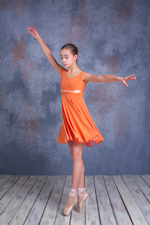 The  young ballerina  in orange dress  dancing in studio on gray backgroundの写真素材