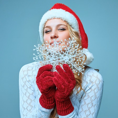 Beautiful young woman in Santa Claus clothes with snowflakes on a blue backgroundの写真素材