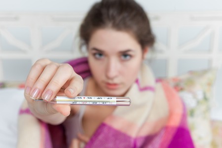 Young sick woman in blanket with  thermometer in bed at home