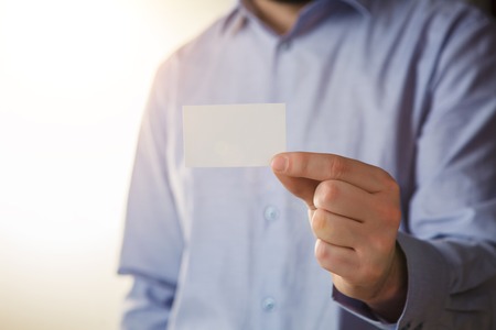 Man holding white business card on white wall backgroundの写真素材