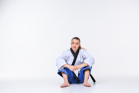The karate girl in white kimono and black belt sitting over white background.の写真素材