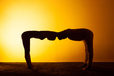 The two silhouettes of people practicing yoga in the sunset light