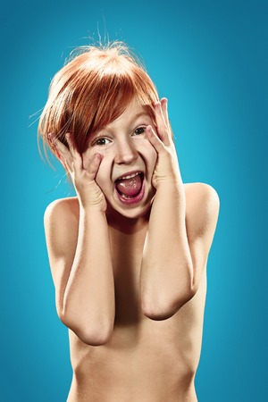 The beautiful portrait of a happy little surprised girl with red hair  on blueの写真素材