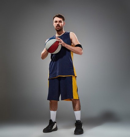 Full length portrait of a basketball player posing with a ball  against gray studio backgroundの写真素材