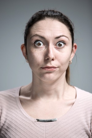 Portrait of young woman with shocked facial expression  over gray backgroundの写真素材