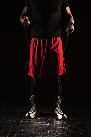 The legs of muscular man with skipping rope training kickboxing  on black