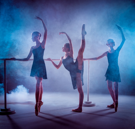 The silhouettes of young ballerinas stretching on the bar on blue smoke backgroundの写真素材