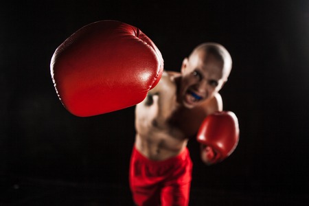 The young male athlete kickboxing on a black background  with kapa in mouth. concept fury in the fightの写真素材