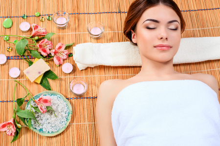 Beautiful young woman at a spa salon resting on a straw mat. Concept of body care and relaxationの写真素材