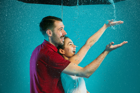 The loving couple in the rain with umbrella on a turquoise backgroundの写真素材