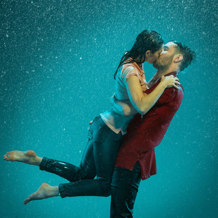 The loving couple kissing in the rain on a turquoise backgroundの写真素材