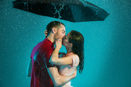 The loving couple in the rain with umbrella on a turquoise backgroundの写真素材