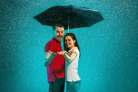 The loving couple in the rain with umbrella on a turquoise backgroundの写真素材
