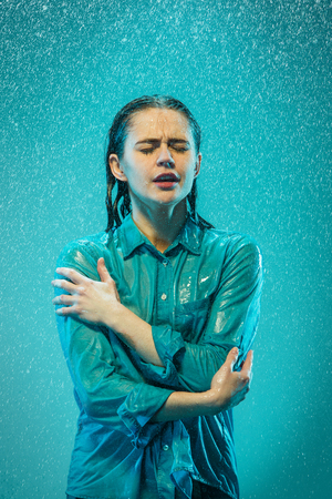 The portrait of young beautiful woman in the rain. The girl standing on a turquoise backgroundの写真素材