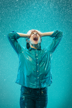 The portrait of young beautiful woman in the rain. The girl screaming on a turquoise backgroundの写真素材