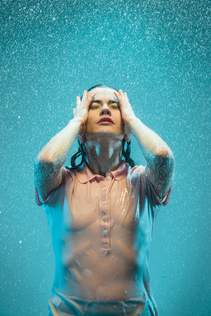 The portrait of young beautiful woman in the rain. The girl standing on a turquoise backgroundの写真素材
