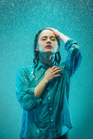 The portrait of young beautiful woman in the rain. The girl standing on a turquoise backgroundの写真素材