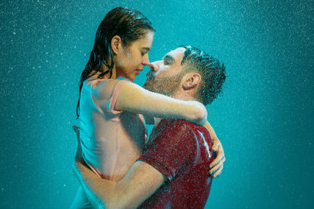 The loving couple kissing in the rain on a turquoise backgroundの写真素材