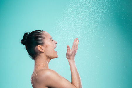 Woman enjoying the water in the shower under a water jet on blue backgroundの写真素材