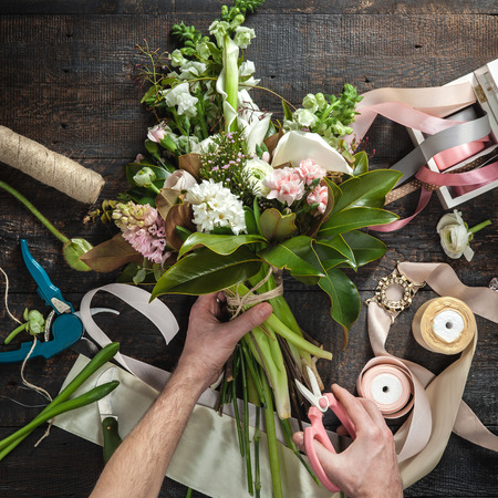The hands of florist against desktop with working tools and ribbons on wooden backgroundの写真素材