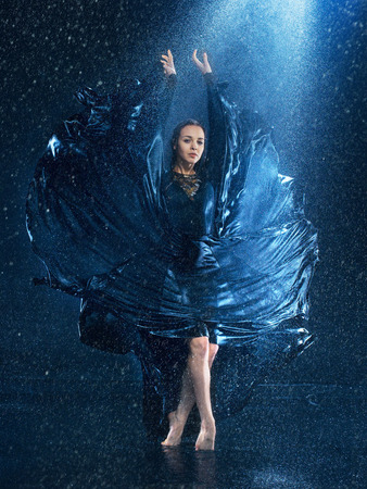 The young beautiful modern dancer in long dress dancing under water drops in blue aqua studioの写真素材