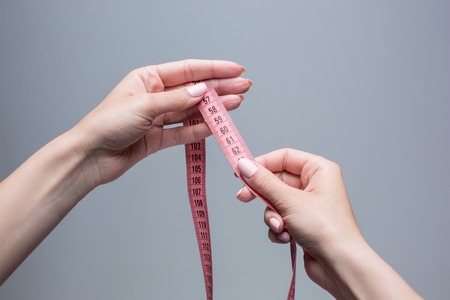 The tape in female hands on gray background. Weight loss, diet and detox conceptの写真素材