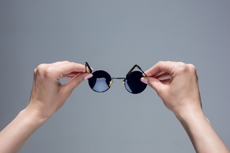 The female hands holding pair of sunglasses on gray background.の写真素材