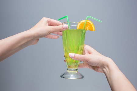 The female hands with cocktail on a gray background