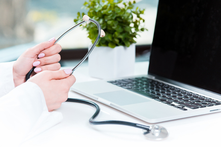 The female doctor with a stethoscope in the hands against laptopの写真素材