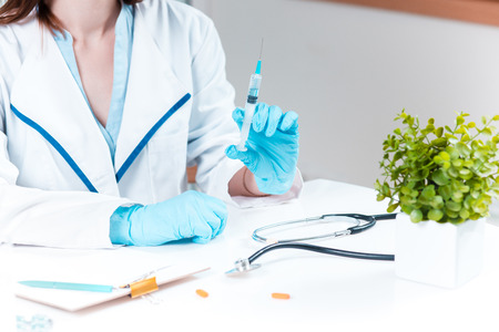 The hand of female doctor in blue glove holding syringe against white medical gownの写真素材