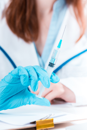 The hand of female doctor in blue glove holding syringe against white medical gownの写真素材