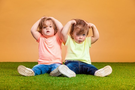 Happy funny girl twins sisters sitting on grass and orange backgroundの写真素材