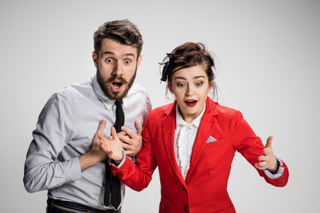 The funny surprised business man and woman smiling on a gray background.