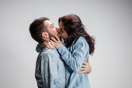 Portrait of happy couple kissing on gray background.