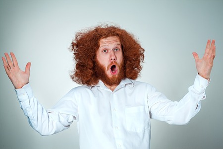 Portrait of young man with long red hair and with shocked facial expression on gray backgroundの写真素材