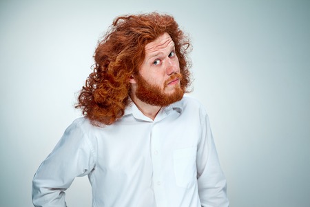 Portrait of young man with long red hair and with shocked facial expression on gray backgroundの写真素材