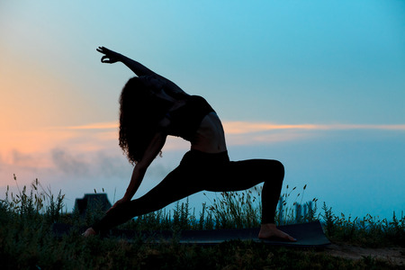 Silhouette of young woman is practicing yoga at sunsetの写真素材