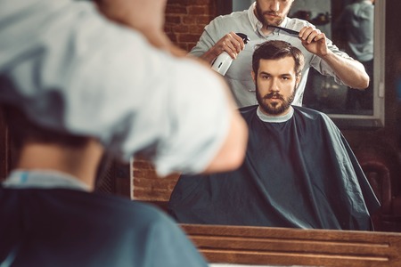 Young handsome barber making haircut of attractive bearded man in barbershopの写真素材