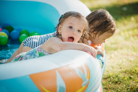 The two Two-year old little baby girls playing with toys in inflatable pool in the summer sunny dayの写真素材