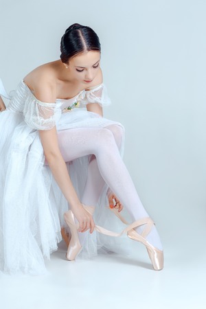 Professional ballerina putting on her ballet shoes on the gray backgroundの写真素材