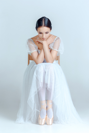 Professional ballerina resting after the performance and sitting with her ballet shoes on the gray backgroundの写真素材