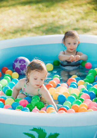 The two Two-year old little baby girls playing with toys in inflatable pool in the summer sunny dayの写真素材