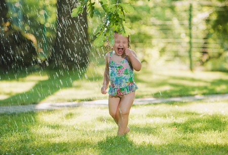 The little baby girl playing with garden sprinkler. Summer outdoor water fun and green grass.の写真素材