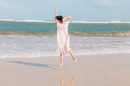The woman with headphones walking on the beach sand and jumpingの写真素材