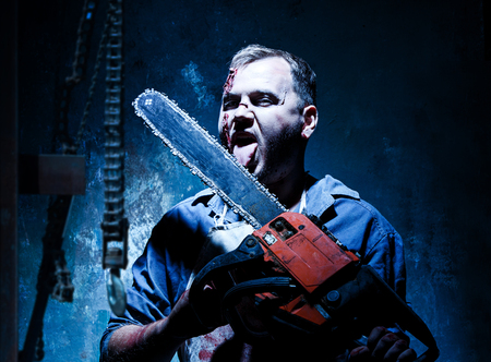 Bloody Halloween theme: crazy killer as bloody butcher with electric saw on dark blue backgroundの写真素材
