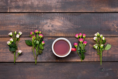 Cup of coffee with roses. The top view on wooden table