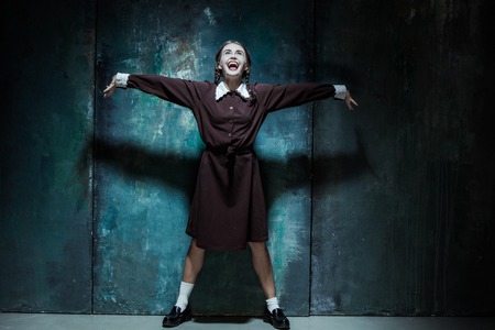 Halloween theme: Portrait of a young smiling girl in school uniform as killer woman against school board . The image in the style of Halloween and Addams familyの写真素材