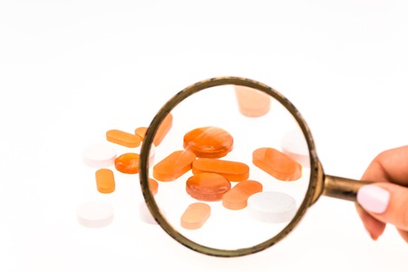 The capsules isolated on the white background and magnifier in female handの写真素材