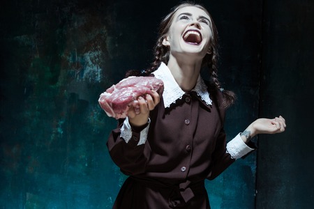Portrait of a young girl with a piece of raw meat. Girl in school uniform as killer. The image in...